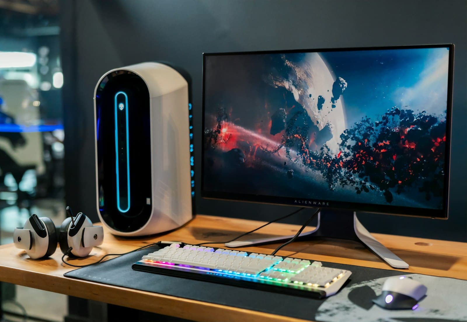 A desktop PC beside a widescreen monitor on a desk, lit by the screen