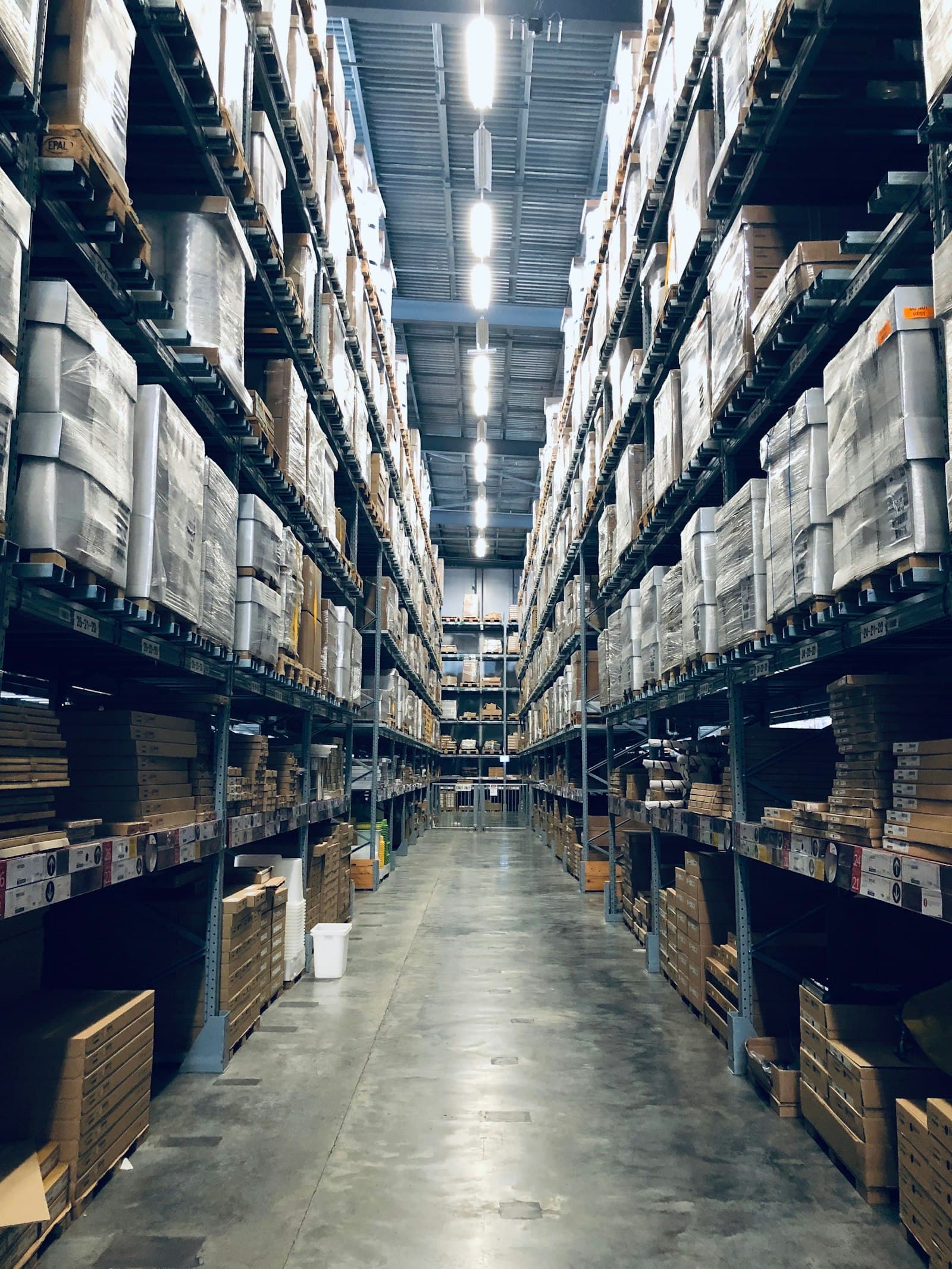 A distribution warehouse aisle, racking stacked with boxed stock to the ceiling